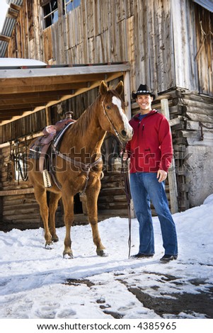 Mid-adult Caucasian male holding his horse with stable in background.
