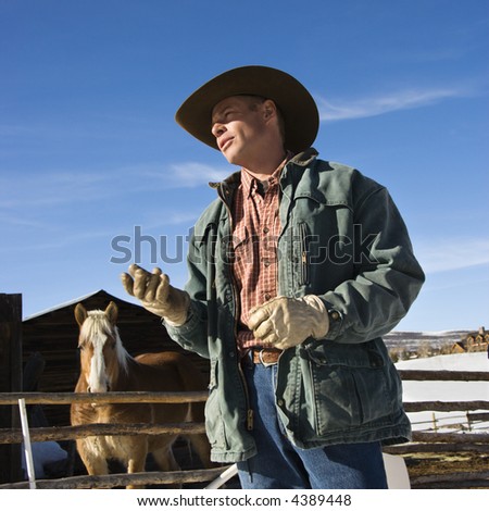 Middle-aged Caucasian male wrangler with horse in background.
