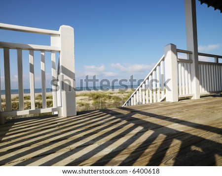 View of beach from porch with railing casting shadow on wooden deck at Bald Head Island, North Carolina