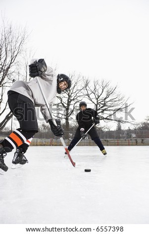 Two boys in ice hockey uniforms skating on ice rink moving puck.