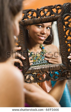 African American mid adult woman smiling at reflection in mirror wearing necklace.