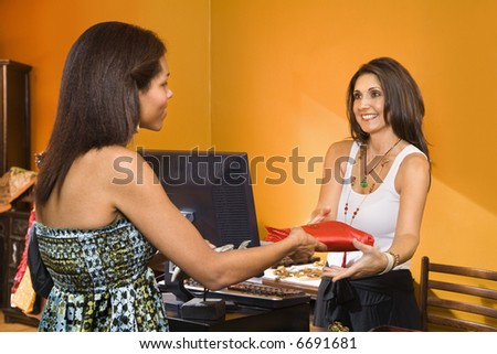 African American women handing item to sales clerk in boutique.