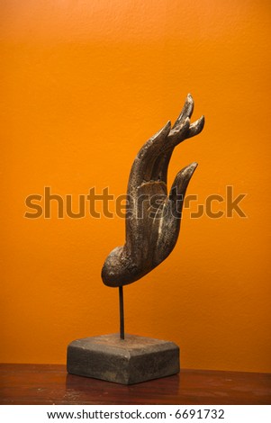 Carved hand sculpture from Thailand against orange wall.