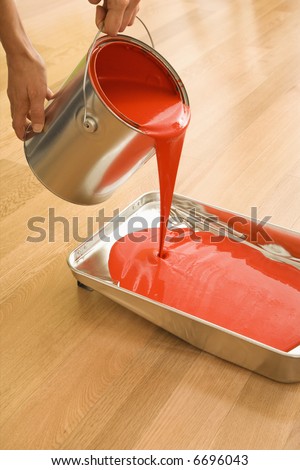 Caucasian woman pouring red paint from can into tray.