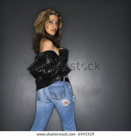 Sexy Caucasian woman taking off leather jacket looking over shoulder at viewer.