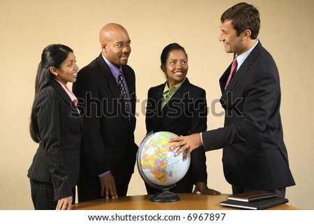 Corporate businesspeople standing around world globe smiling and talking.