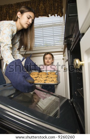 Caucasian mother and daughter  taking cookies out of oven.