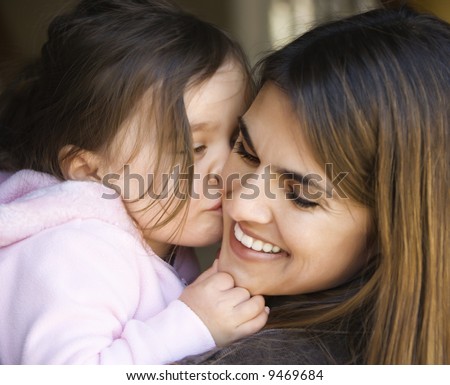 Caucasian mother holding daughter kissing her cheek and smiling.