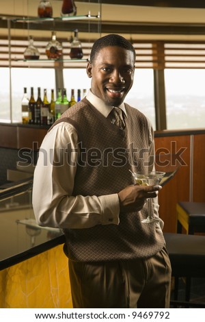 African American mid adult man at bar with martini smiling at viewer.