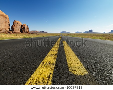 Open highway in scenic desert landscape with distant mountains and butte land formations.