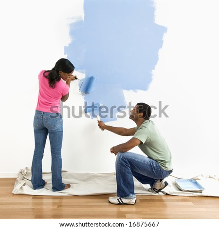 Smiling African American male and female couple painting wall blue.