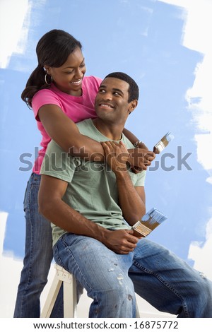 Portrait of African American male and female couple next to half-painted wall.