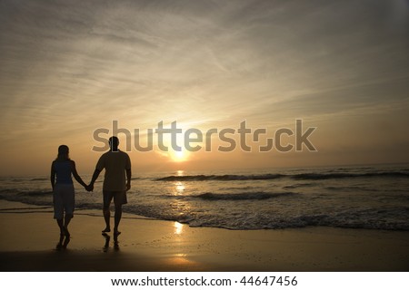 Silhouette of couple walking on beach at sunset holding hands. Horizontally framed shot.