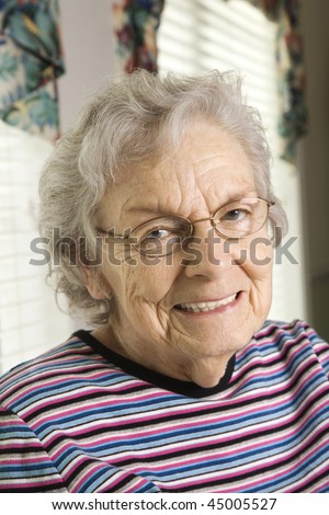 Elderly woman in glasses smiles towards the camera.  Vertical shot.
