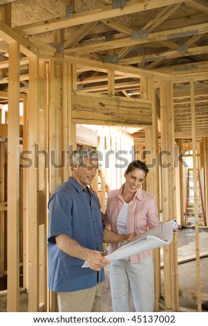 Couple go over home building plans at a construction site. Vertical shot.