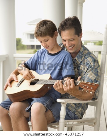 Son sits on his father\'s lap while playing guitar. Vertical shot.