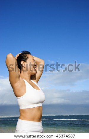Side view of an Asian woman smiling with hands on her head standing on Maui Hawaii beach. Vertical shot.