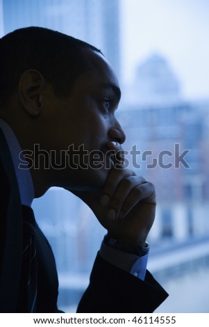 Close-up profile of an African-American mid-adult businessman with hand on chin in front of window. Vertical format.