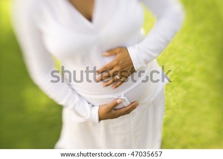 High angle view of the torso of a pregnant woman with her hands on her belly. Horizontal shot.