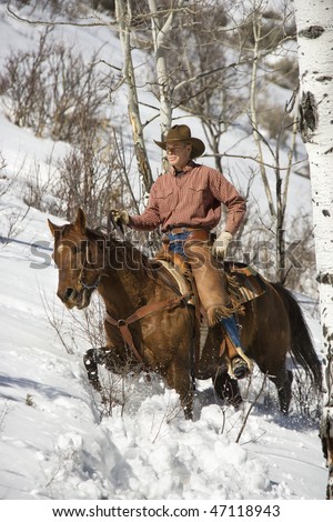 Cowboy in chaps riding a horse in the snow. Vertical shot.