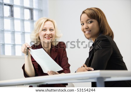Businesswomen sitting at office desk going over paperwork.