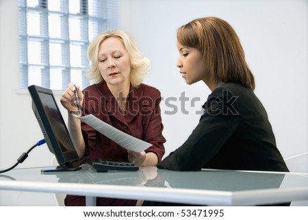 Businesswomen sitting at office desk going over paperwork.