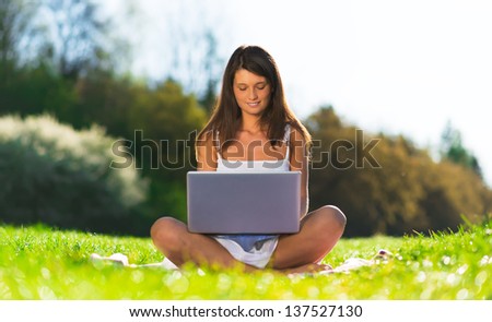 Pretty girl sitting at the country side using a laptop