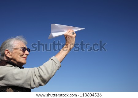 Senior woman playing with paper plane over blue sky.
