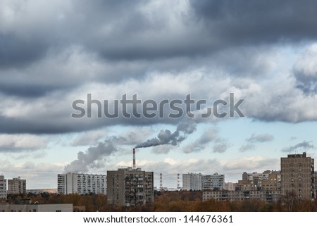 Smokestacks polluting cloudy sky with smoke over industrial city cityscape.