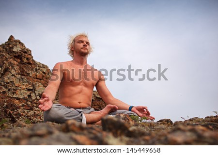 Young adult man sitting on mountain in Lotus yoga pose.