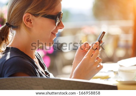 Portrait of happy woman reading off touch phone in cafe outdoors.