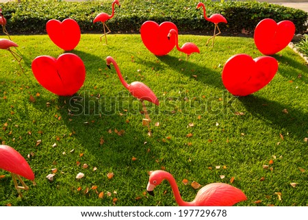 Red love hearts and flamingo birds installed on green lawn.