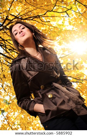 Beautiful young woman under tree branches with yellow autumn foliage in park, blowing a kiss.