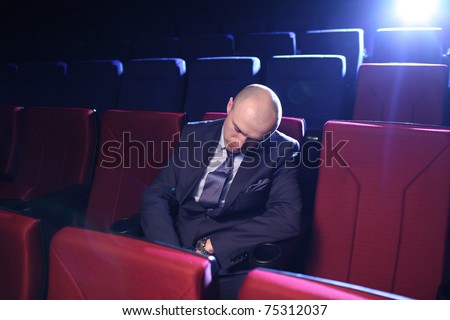 Bald man sleeping in empty movie theater.