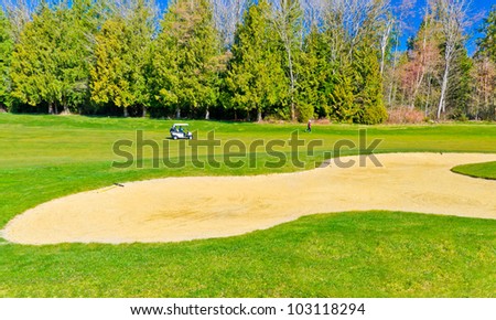 Sand bunker on the golf course with the golf cart on the meadow .