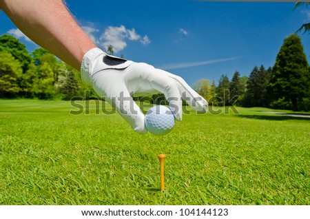 Hand wearing golf glove placing golf ball on the tee over beautiful golf course with blue sky