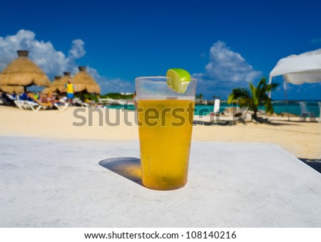 Glass with icy lemonade   ( beer, ice tea ) on the tropical beach with a resort as a background.