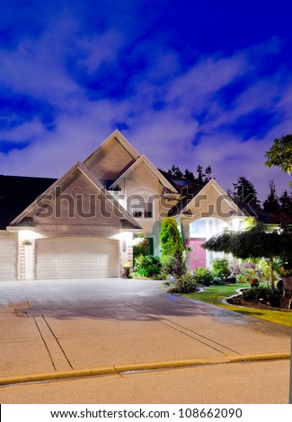 Fragment of a big luxury house with the triple garage doors at dusk, night time.