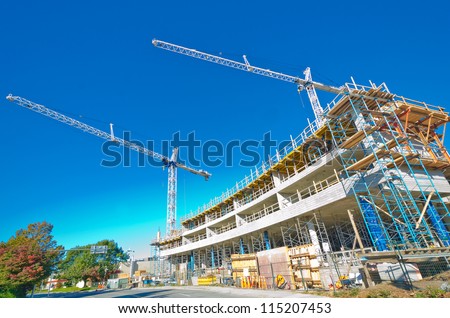 High-rise building under construction. The site with cranes against blue sky. Vancouver, Canada.