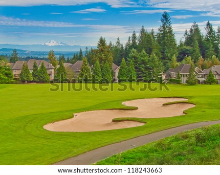 Great view at the golf course with gorgeous green and sand bunker and dark blue sky with white clouds as a background.