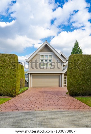 Big custom made double doors garage with nicely paved long driveway and trimmed bushes aside in the suburbs of Vancouver, Canada.