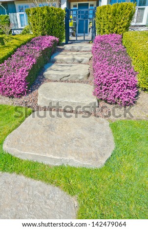 Nicely stoned and paved house doorway, trail with some flowers and trimmed bushes aside steps. Landscape design. House entrance.