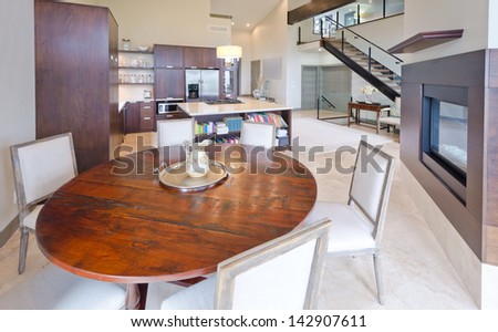 Luxury spacious modern dining room with the table and chairs and the kitchen, fireplace and the stairs to the upper level at the back. Interior design.