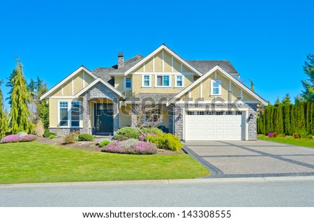 Big custom made luxury double garage doors house with nicely trimmed and landscaped front yard and paved driveway in the suburbs of Vancouver, Canada.