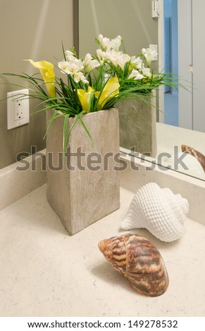 Fragment of nicely decorated modern washroom, bathroom with the vase with some flowers and the shells on the counter. Interior design. Vertical.