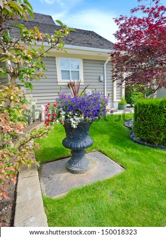Garden vase with nicely decorated colorful flowers and trimmed front yard lawn. Landscape design.