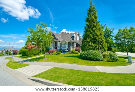 Big custom made luxury house with nicely trimmed and landscaped front yard on the  empty street with pedestrian sidewalk in the suburbs of Vancouver, Canada.