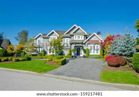 Big custom made luxury house with nicely trimmed and landscaped front yard lawn and long paved driveway  in the suburbs of Vancouver, Canada.