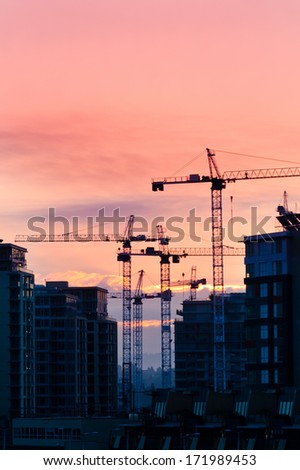 Construction site with cranes at sunset, sunrise, dawn time with the cranes as a silhouette. Vancouver, Canada. Vertical.
