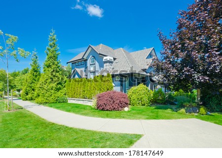 Big custom made luxury house with nicely  trimmed and landscaped front yard on empty street with curved pedestrian sidewalk in suburbs of Vancouver, Canada.